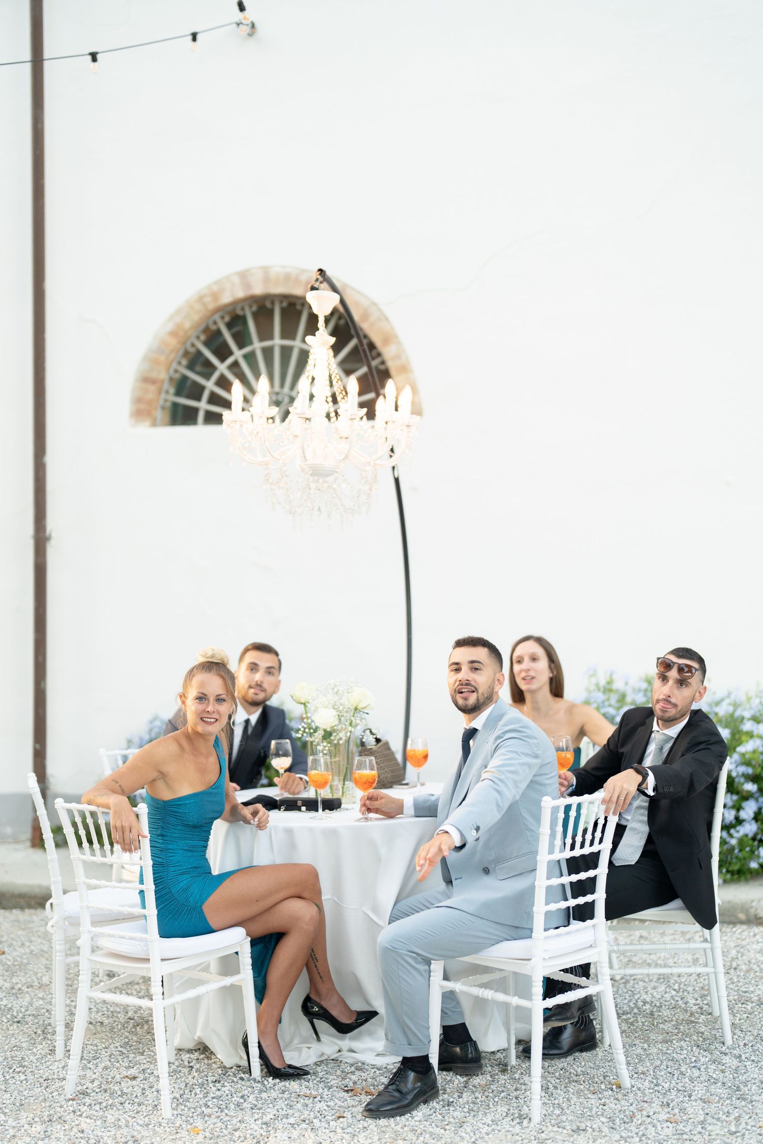 Wedding guests seated at an elegant outdoor table setting with string lights overhead.