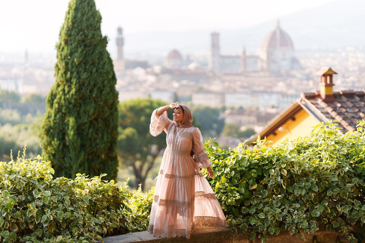 Woman in pink dress poses before Florence skyline with cathedral dome and cypress trees.