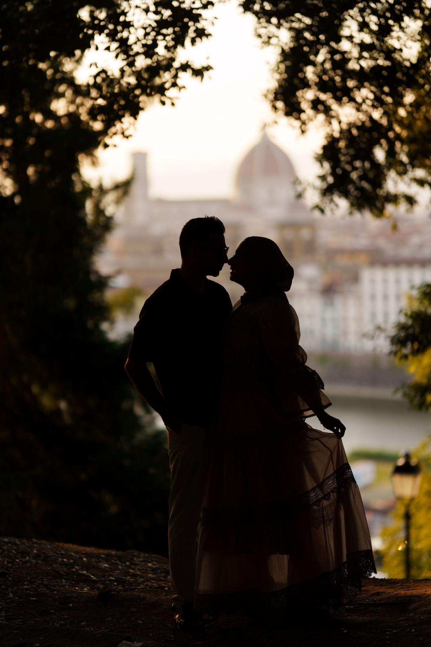 Romantic silhouette of a couple about to kiss with Florence cathedral dome at sunset backdrop.