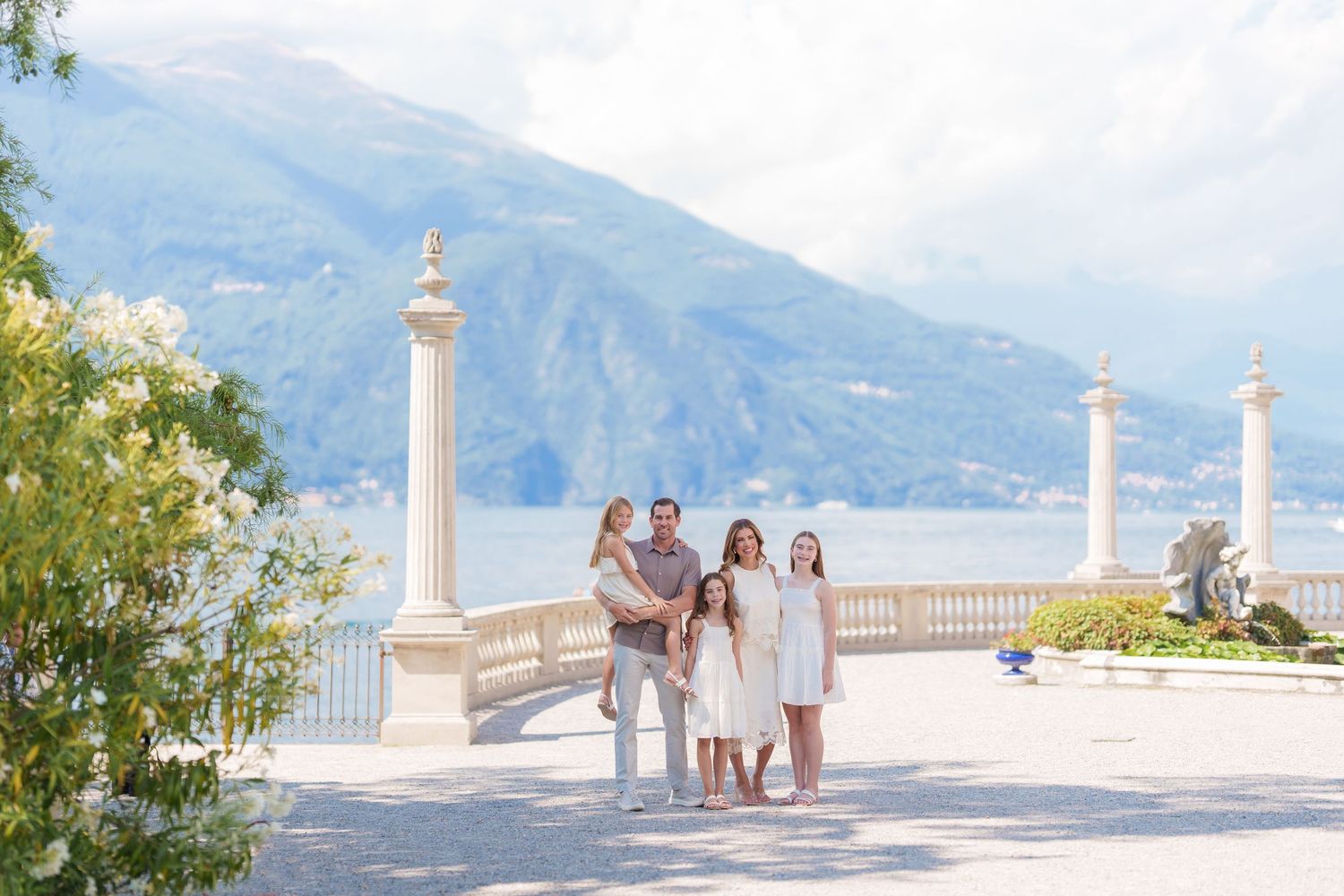 Family of five posing on elegant lakeside terrace with mountain Professional Lake Como family photographer in Bellagio