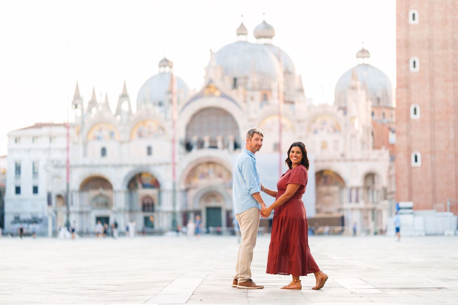 Couple holding hands in St. Mark's Square, Venice, with the iconic Basilica di San Marco in the background.
