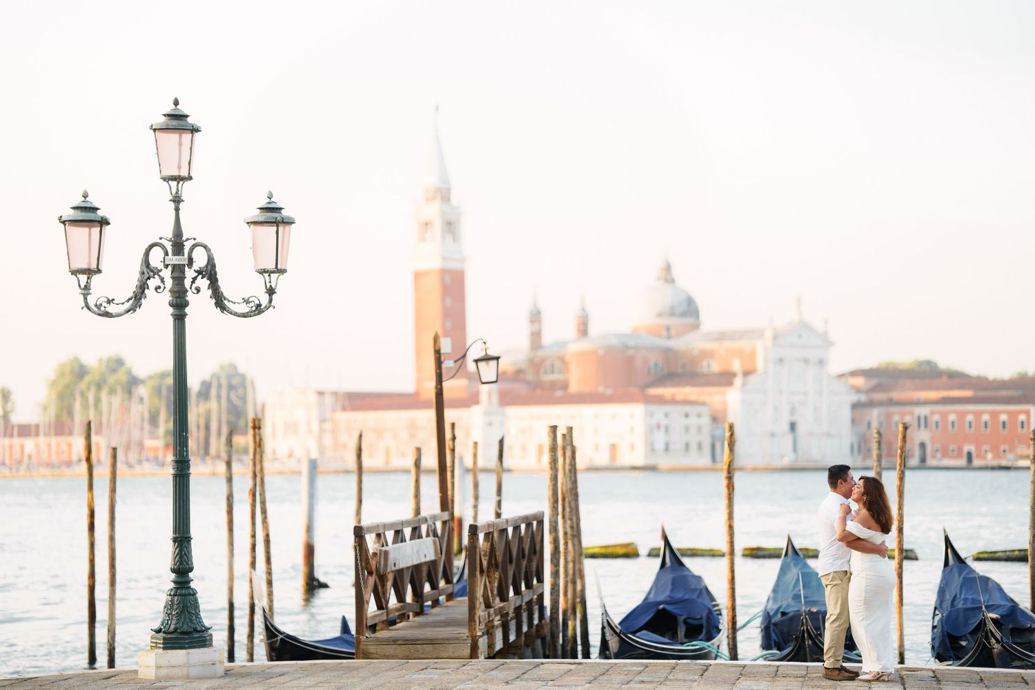 Ornate street lamp and traditional gondolas line the waterfront in Venice with San Giorgio Maggiore church in the background.