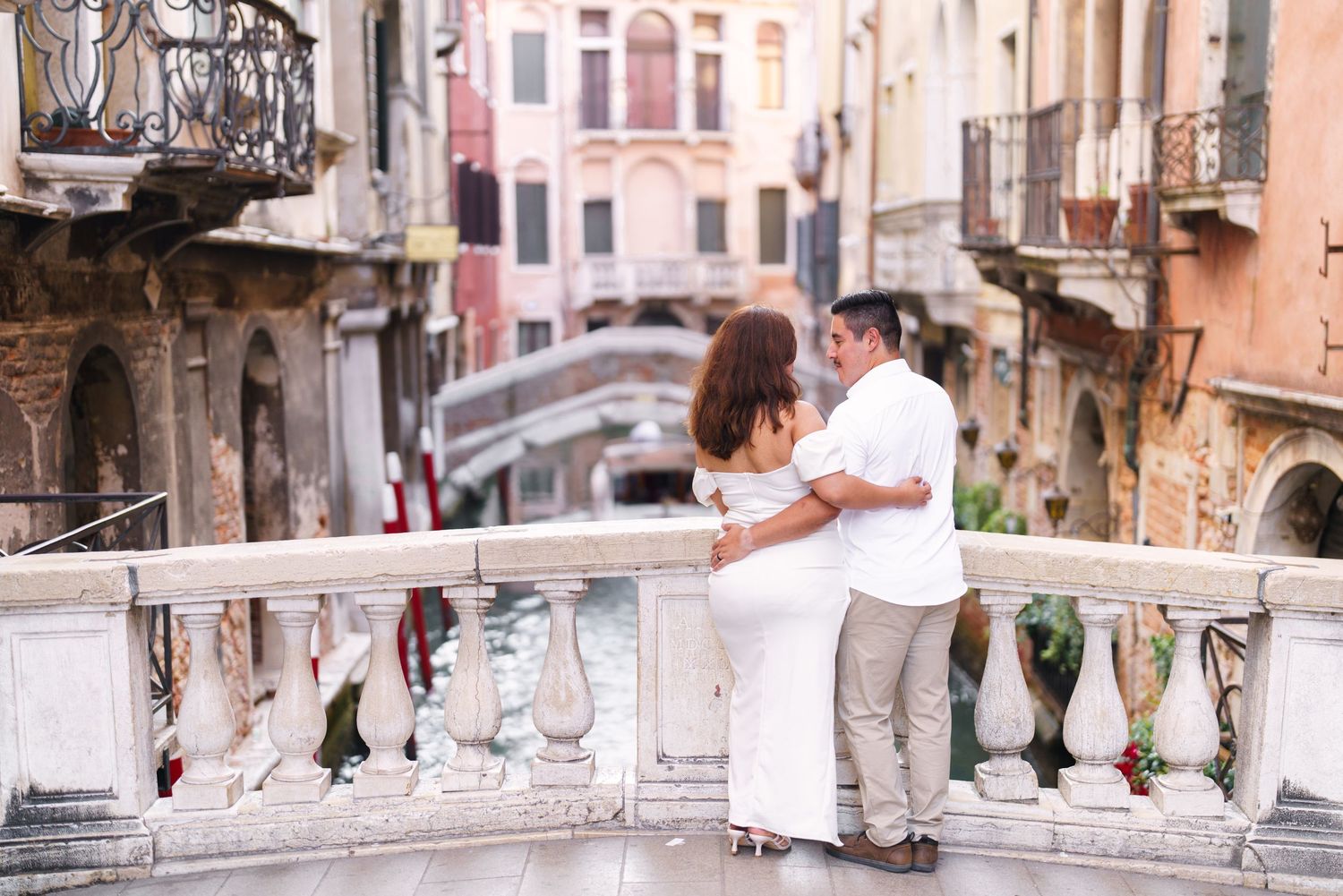 A couple embraces while standing on a romantic Venetian bridge overlooking a canal in Venice, Italy.