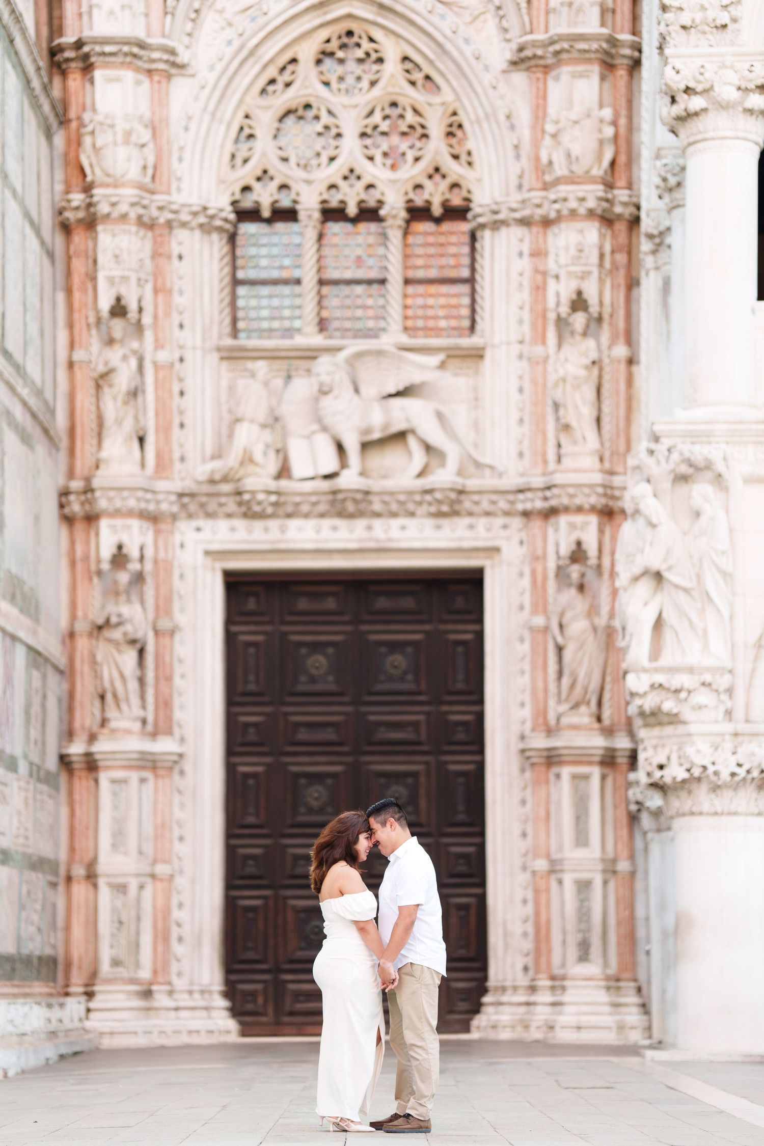 A romantic couple shares tender moments in front of an ornate cathedral with Gothic architectural details.