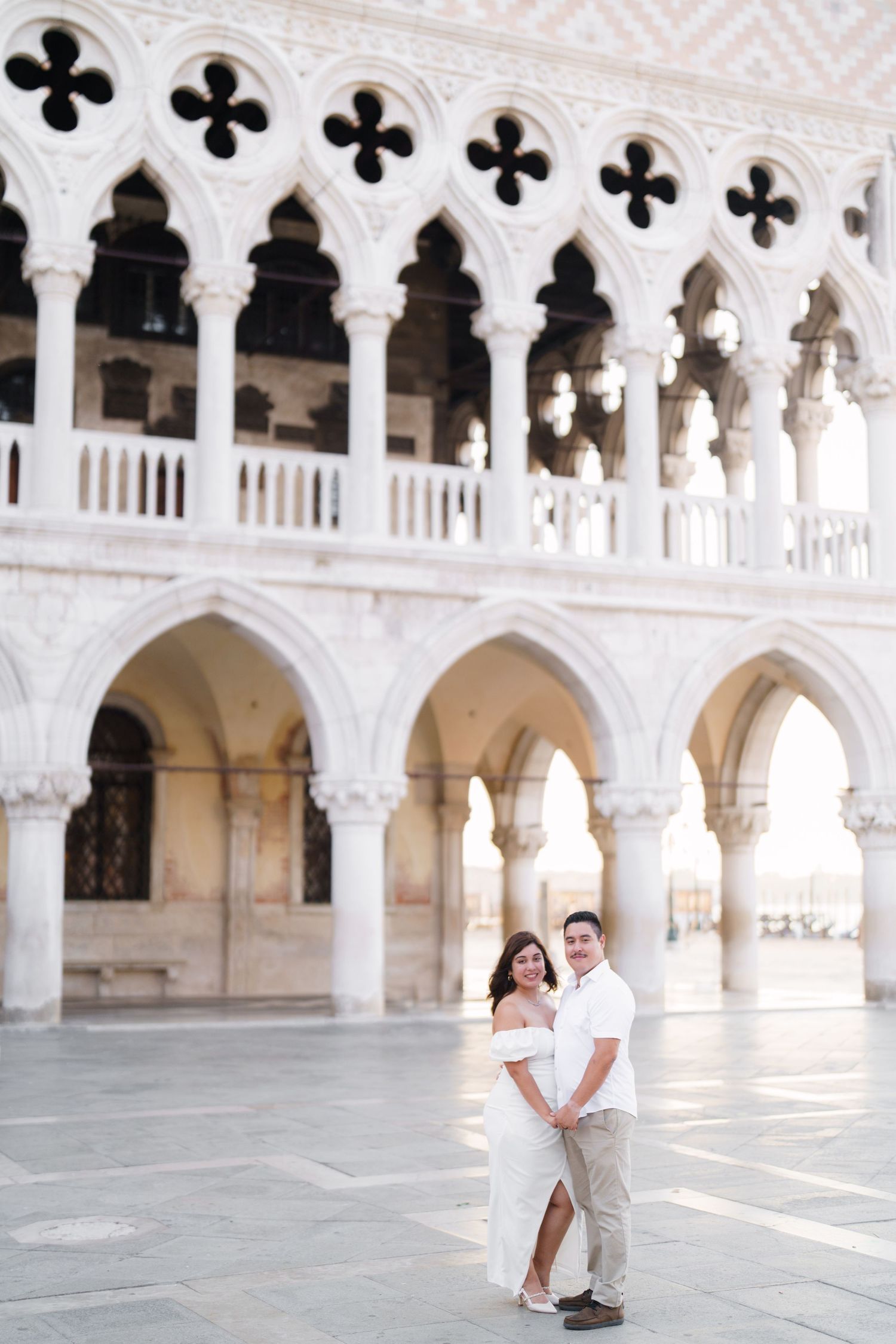 Romantic couple embraces under elegant white marble colonnade in Venice's historic architecture.
