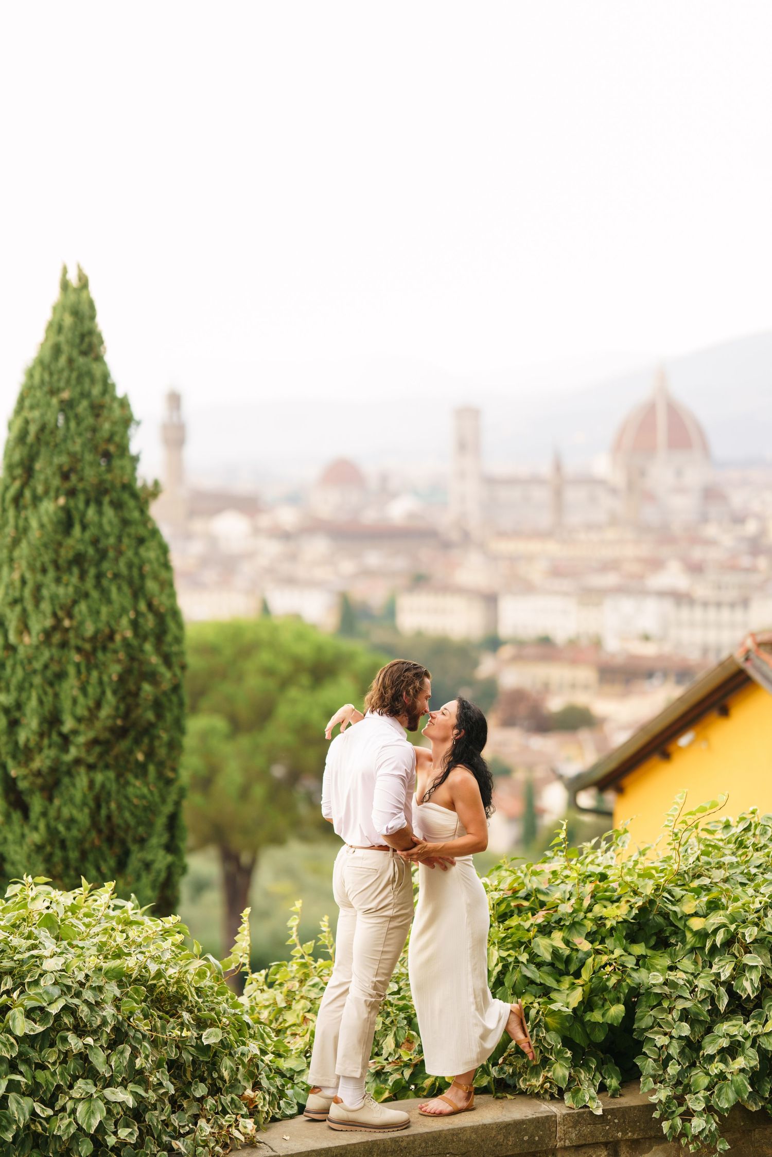 Romantic couple embraces on hillside overlooking the iconic Duomo cathedral and skyline of Florence, Italy.