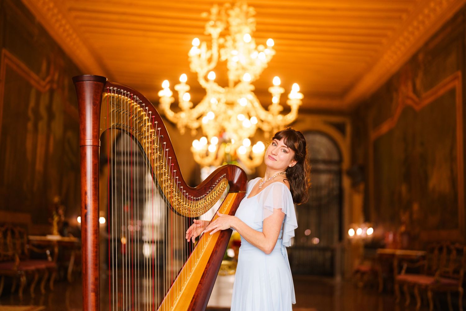 Elegant wedding ceremony in a grand ballroom with ornate chandeliers and a harpist performing in a white dress.