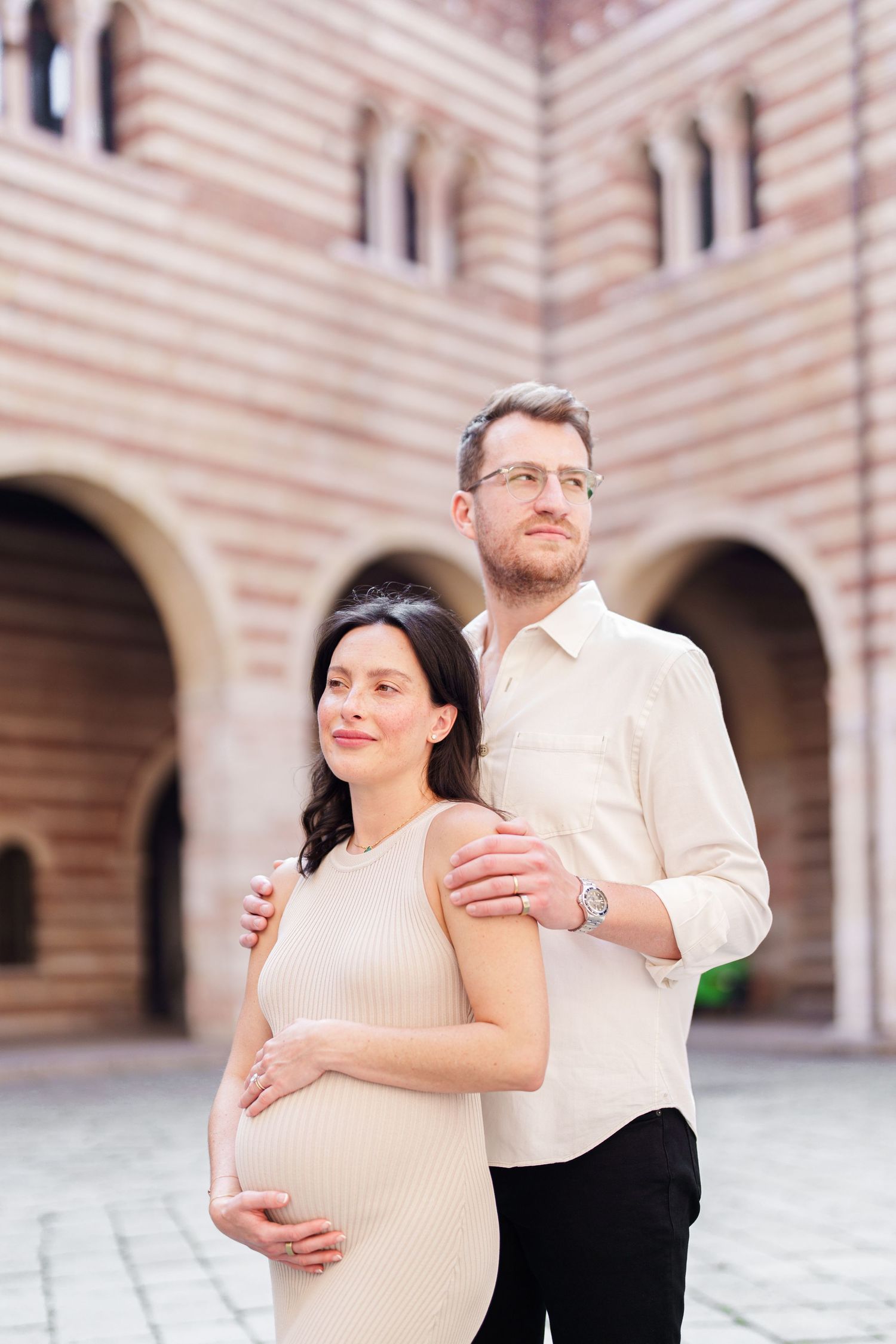 A couple embraces in a romantic photoshoot against a beautiful arched stone building with striped walls.