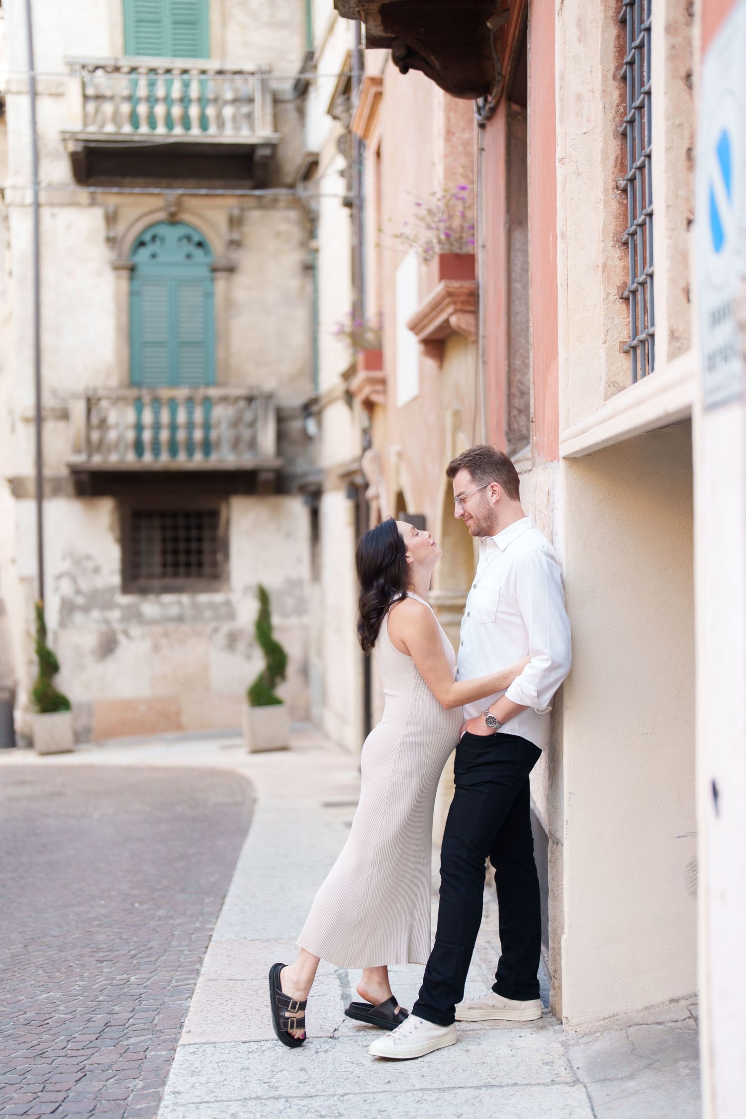 Romantic couple embraces on a charming European cobblestone street with historic architecture and turquoise shutters.