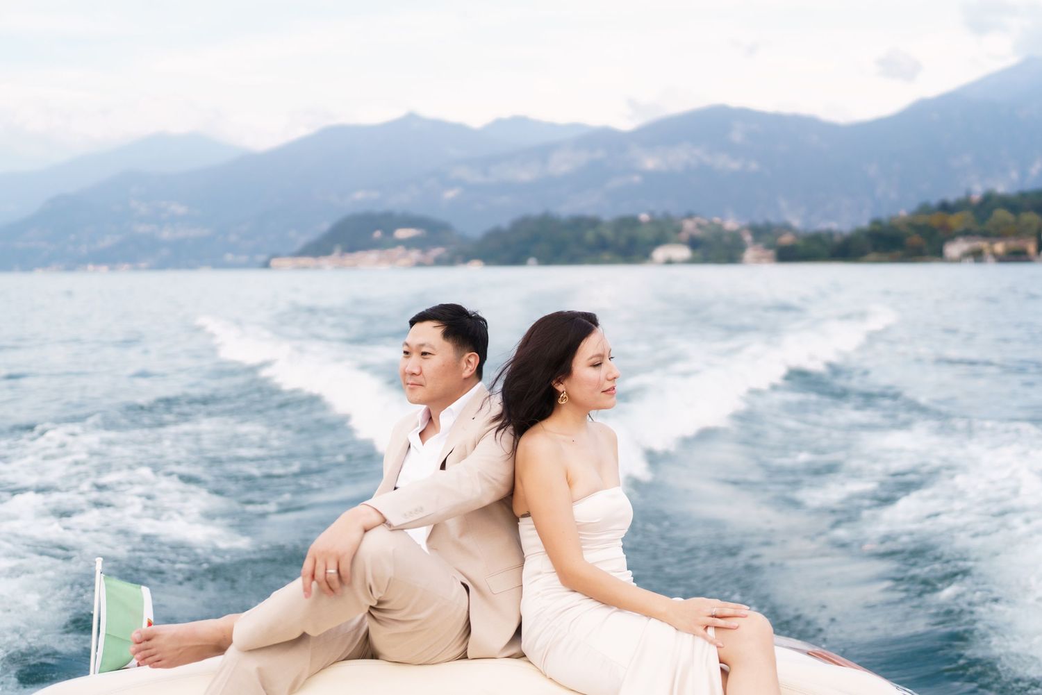 Couple enjoying a romantic boat ride along the coast with mountains and wake trails visible in the water.
