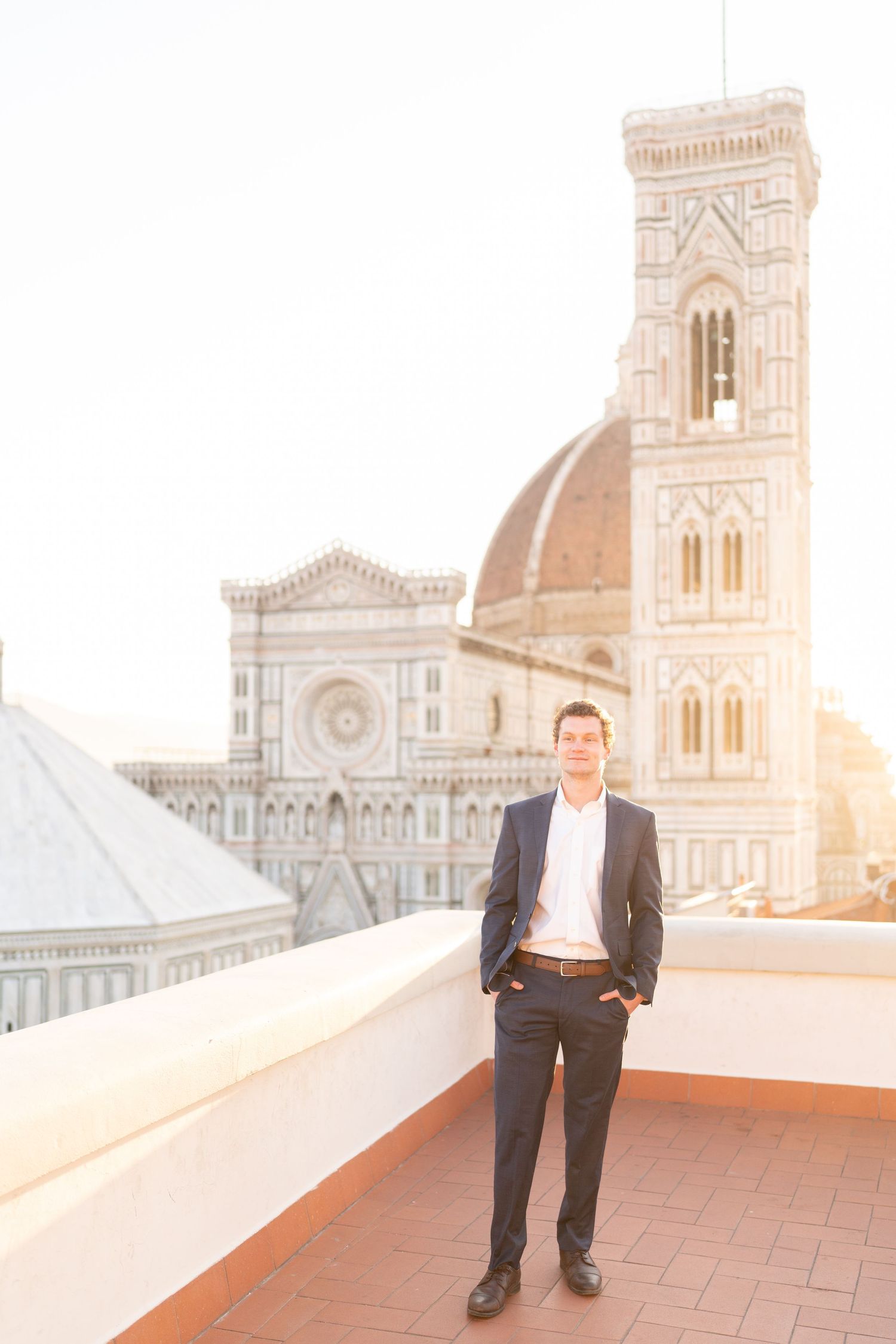 A person stands on a terrace overlooking the historic Florence Cathedral and Giotto's Bell Tower during sunset in Italy.