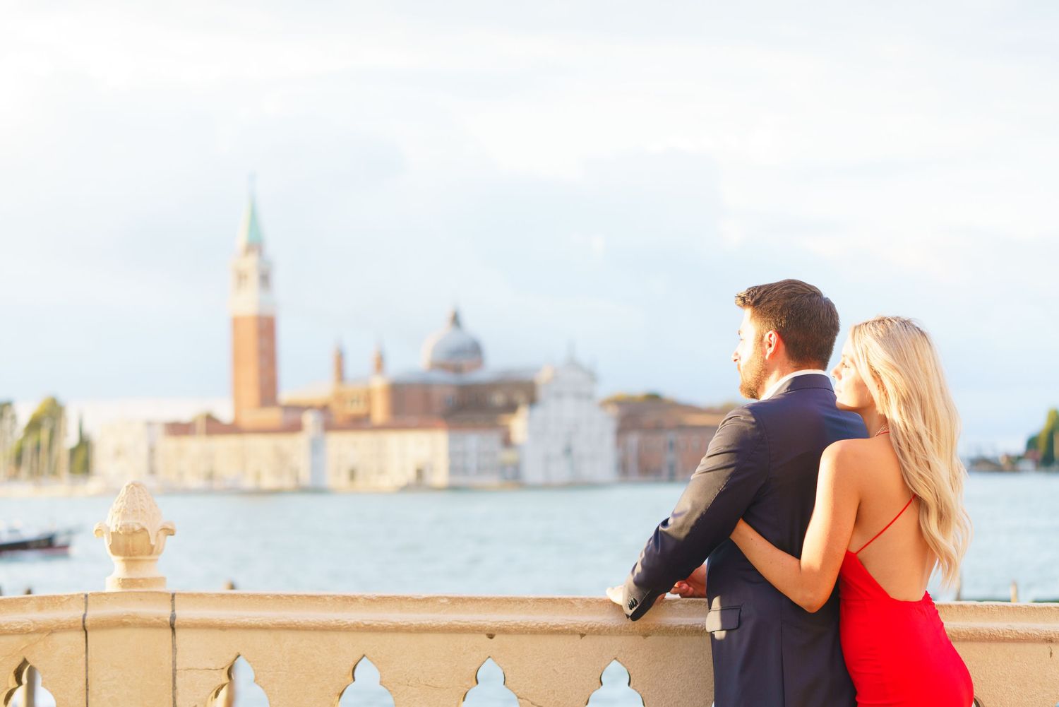 A couple sits on a bench overlooking the Venice lagoon with the iconic San Giorgio Maggiore church in the background.