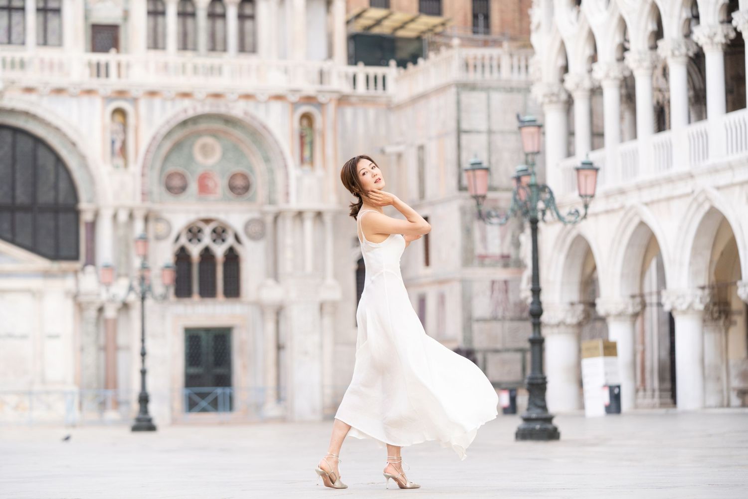 A couple poses in elegant wedding attire against the ornate architecture of Venice's St. Mark's Square.