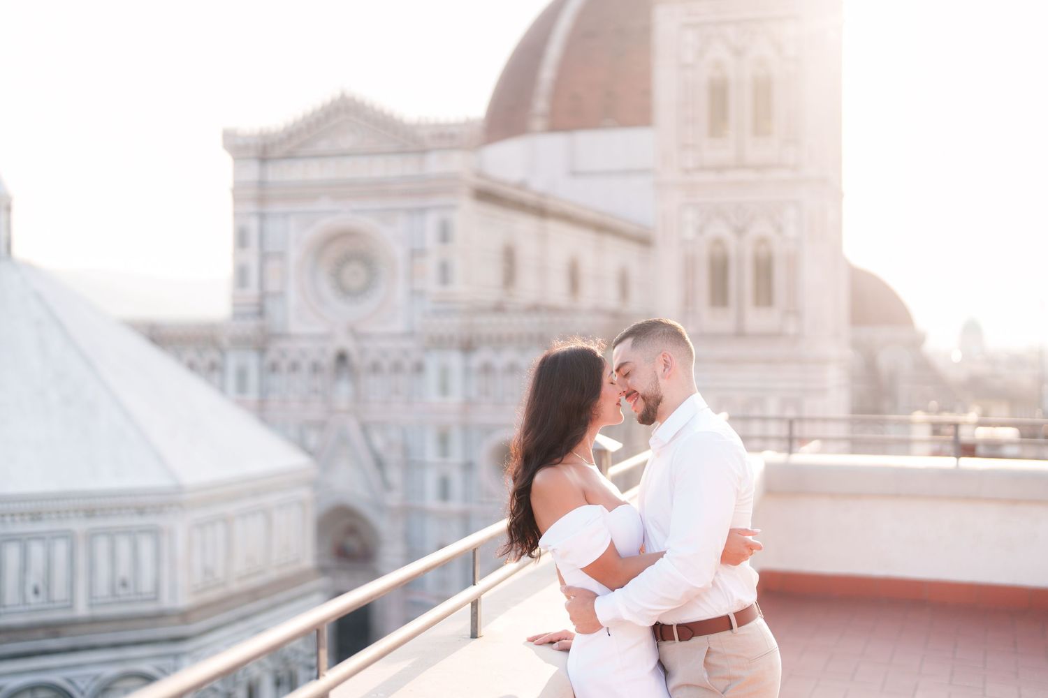 A couple in elegant wedding attire shares romantic moments on a rooftop overlooking Florence Cathedral at sunset.