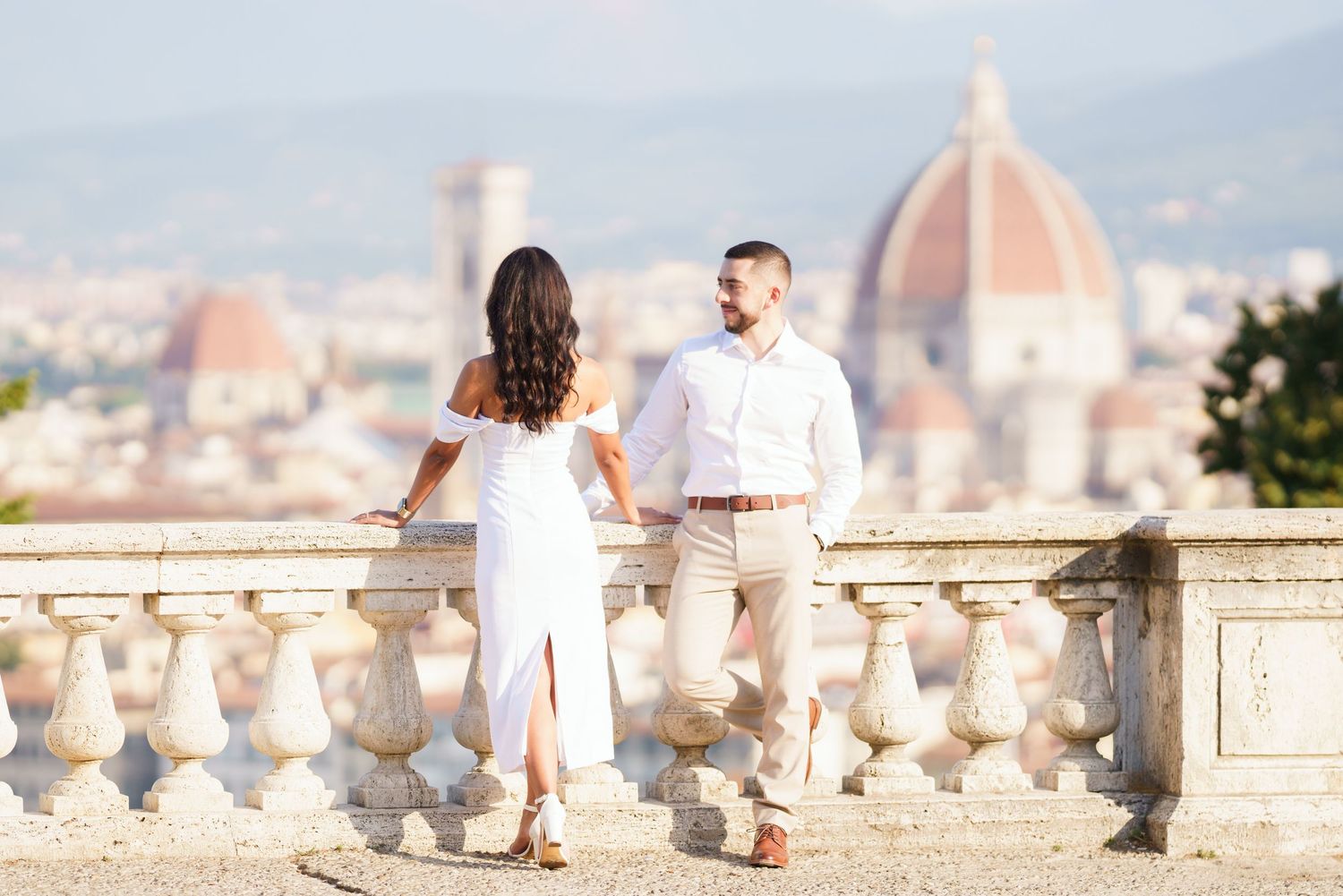 A romantic couple stands on a scenic overlook at Piazzale Michelangelo in Florence, Italy during sunset.