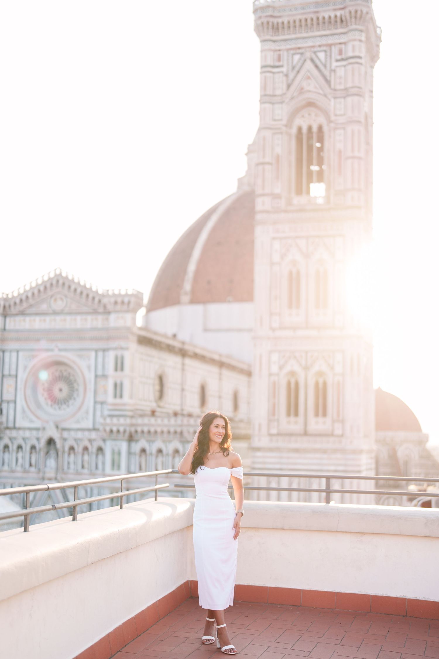 Woman in white dress twirls joyfully on rooftop terrace with Florence Cathedral and historic architecture in background.