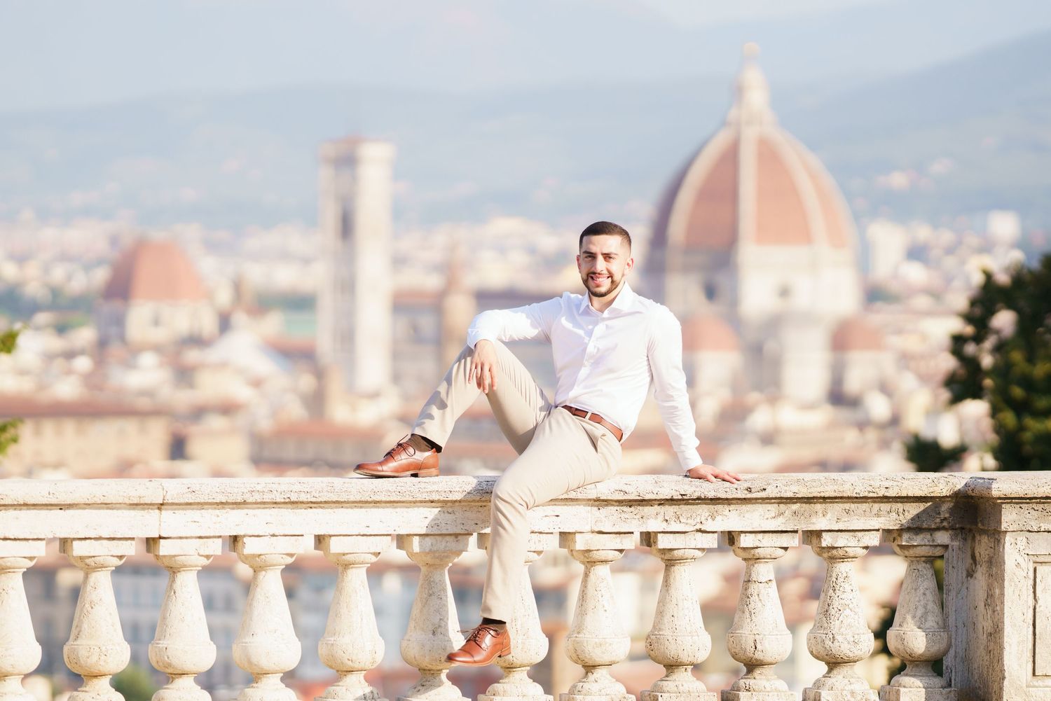 Person in white clothing sits on stone balustrade overlooking Florence with Duomo cathedral visible in background.