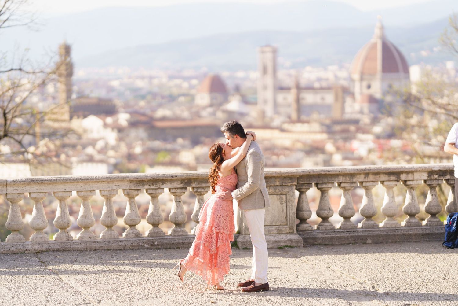 A couple embraces on a scenic overlook with Florence's iconic Duomo cathedral and cityscape in the background.