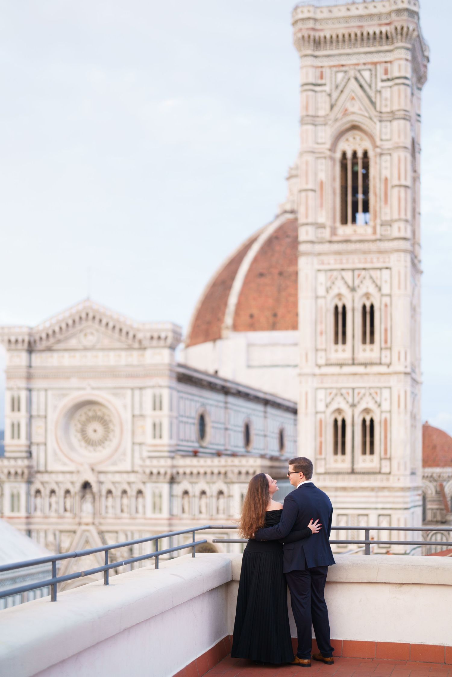 A couple enjoys a romantic moment on a rooftop terrace overlooking the iconic Duomo cathedral in Florence, Italy.
