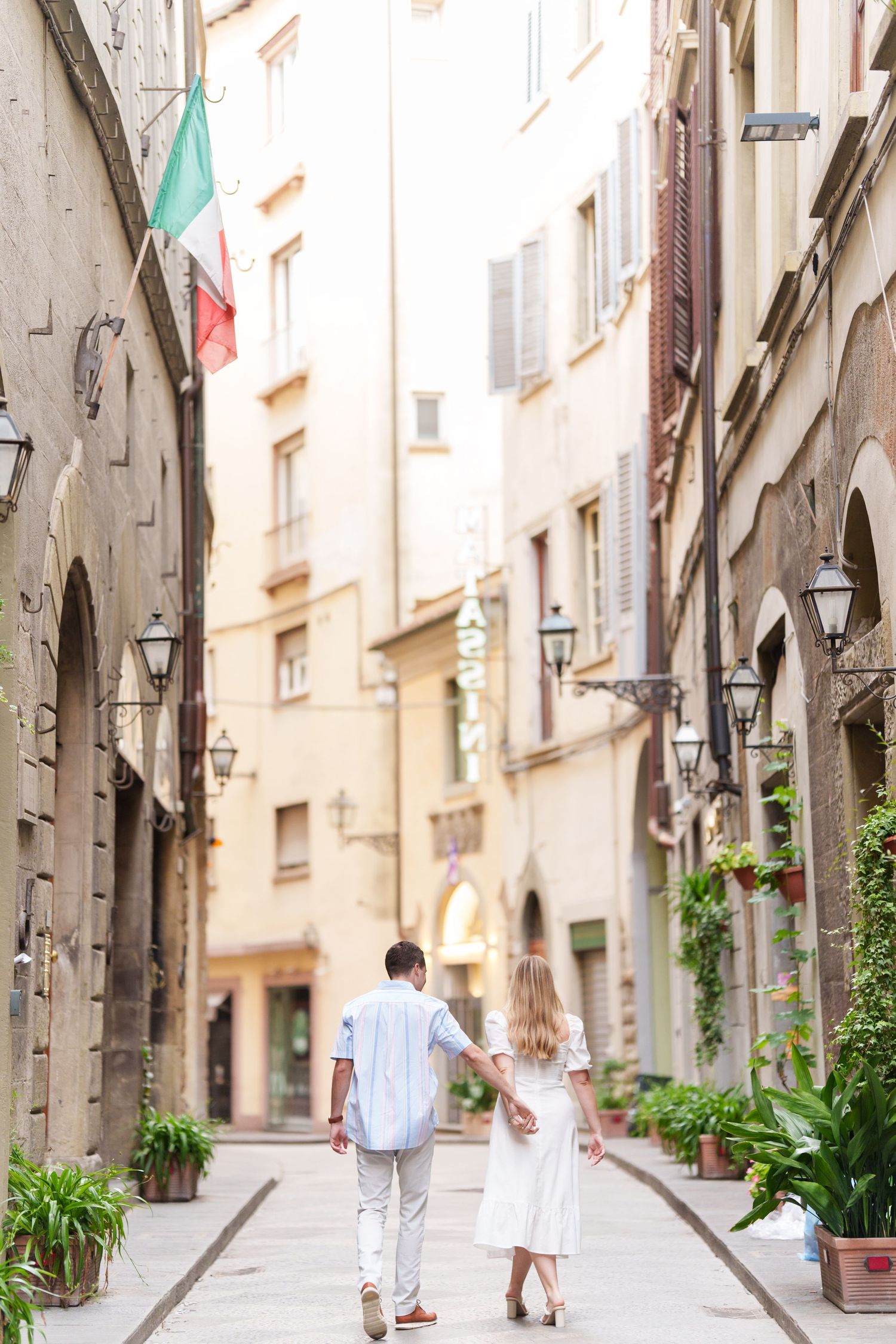 Narrow cobblestone street in historic European city with stone buildings and lanterns along the walls.