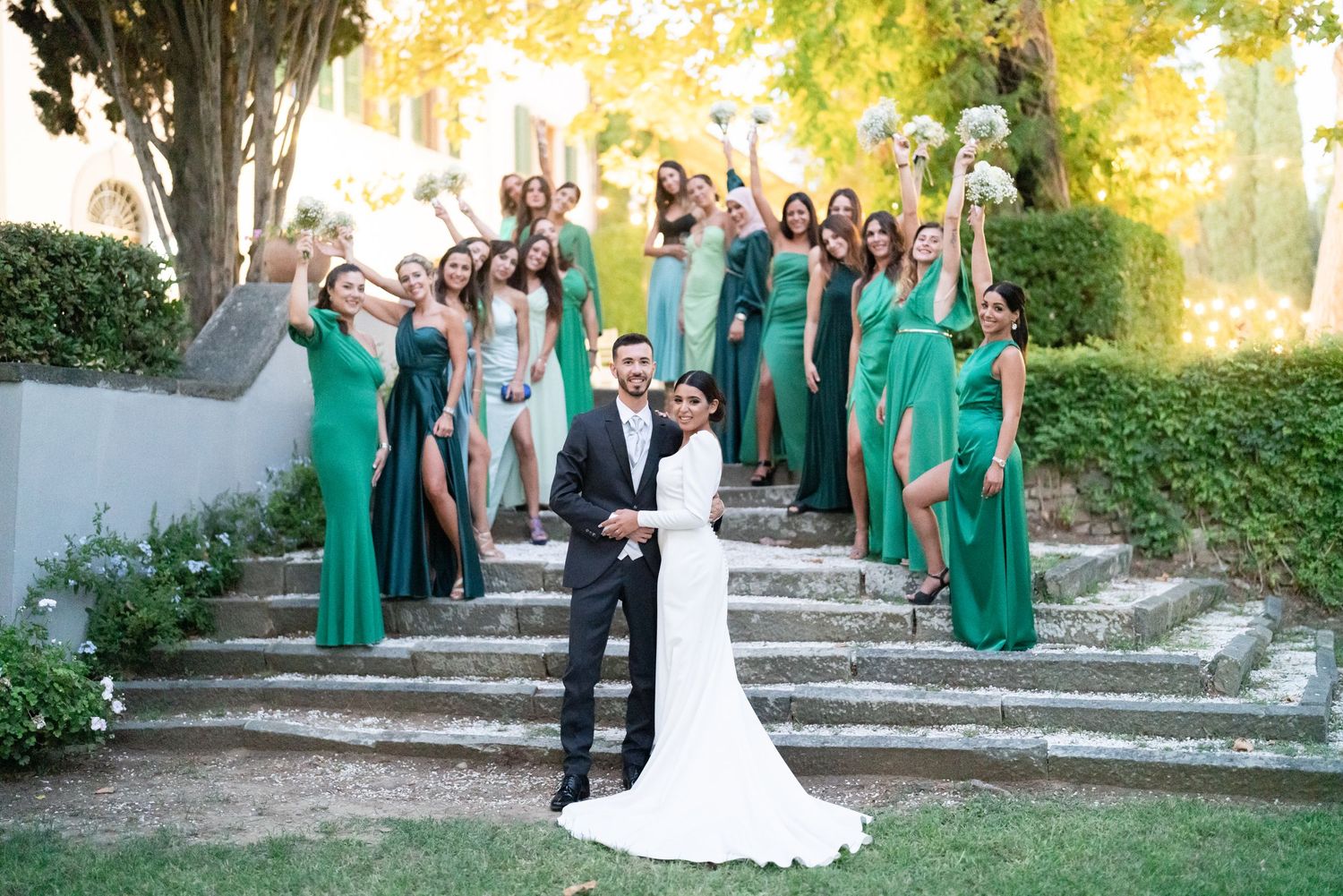 Wedding party in emerald green dresses gathered on stone steps outdoors.