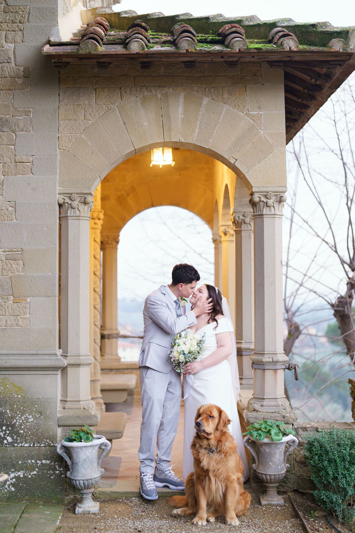 Wedding photos in stone archway with golden retriever sitting beside couple in formal attire.