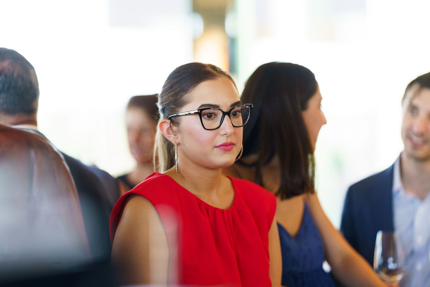 Person in red dress and glasses at social gathering.