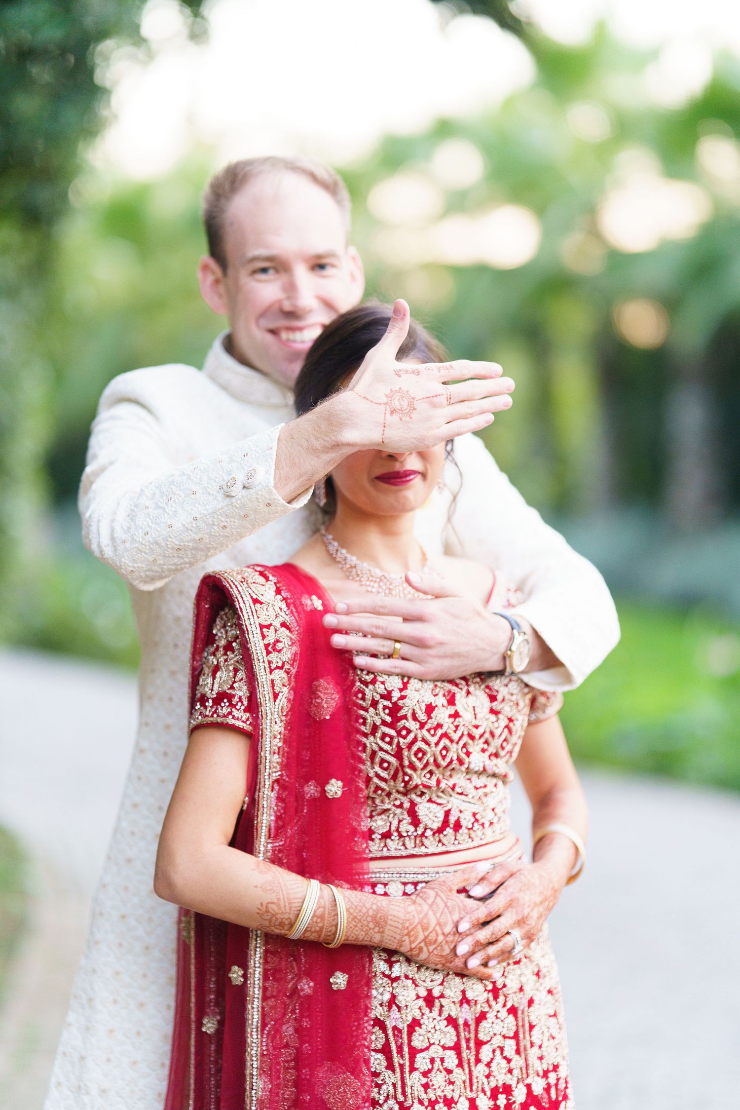 A couple shares playful moments in traditional wedding attire against a garden backdrop.