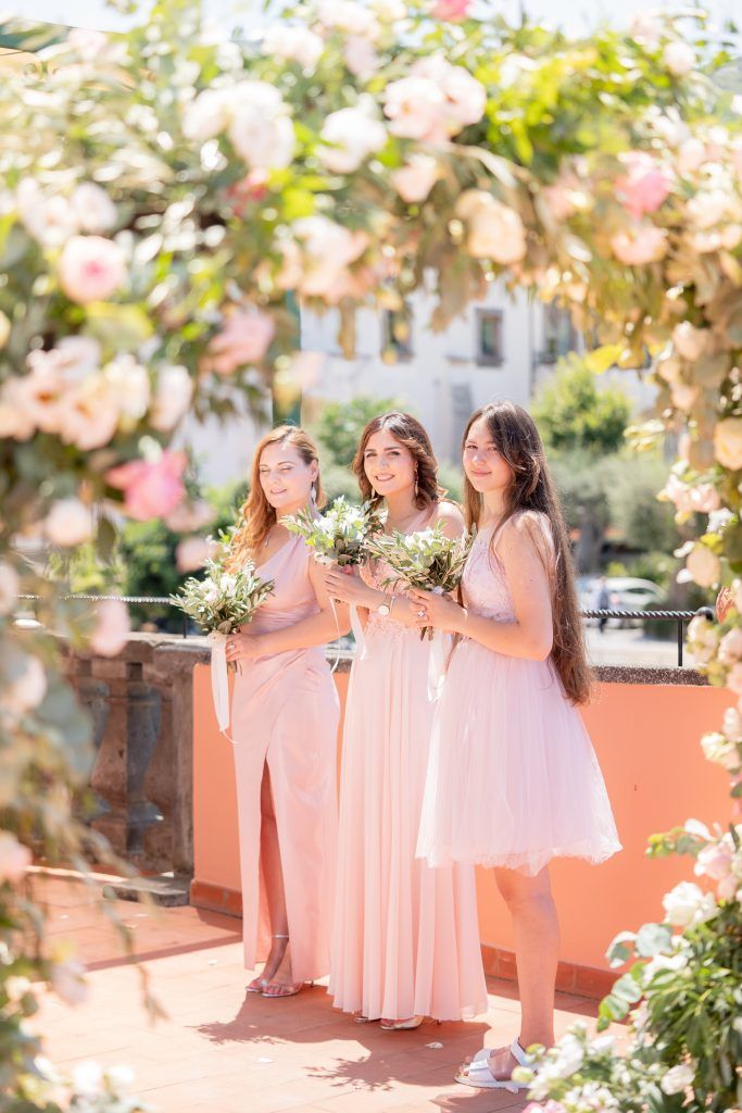 Bridesmaids in flowing peach-colored dresses pose together under flowering trees at an outdoor wedding venue.
