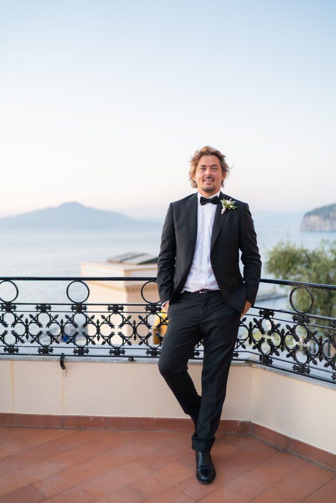 Person in formal attire relaxing on terrace with coastal views.