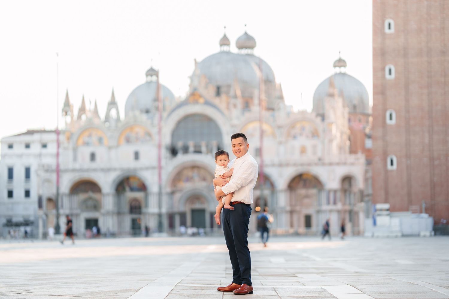 Father holding baby in Piazza San Marco with St. Mark's Basilica in Venice, Italy backdrop.