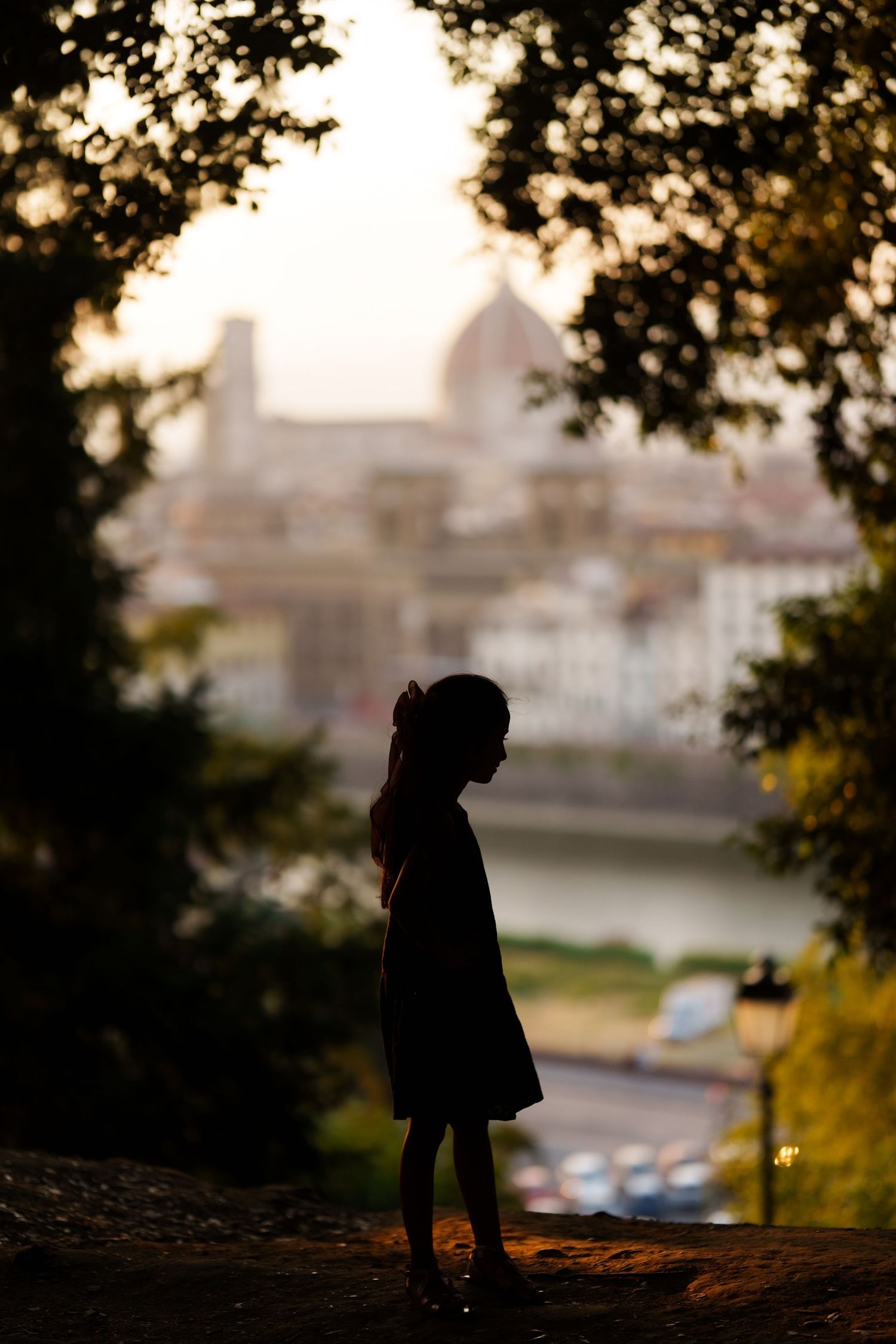 Silhouette of a young girl standing on a hilltop overlooking Florence, Italy at sunset with the Duomo in the background.