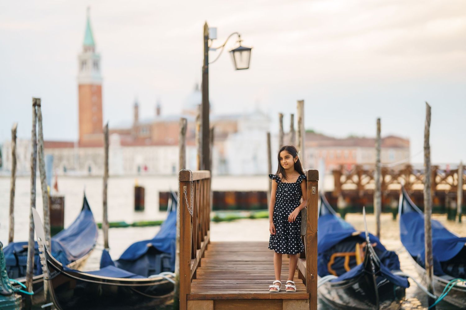 Woman in polka dot dress posing on Venice gondola dock with San Giorgio Maggiore church in background.