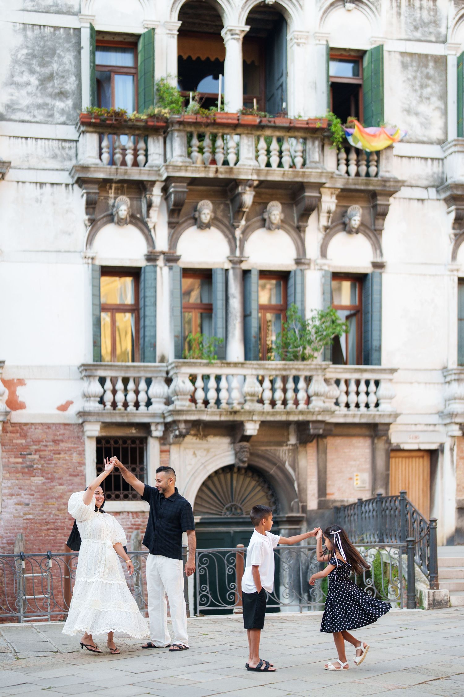 Family dancing together in front of a historic Venetian building with ornate balconies and arched windows.