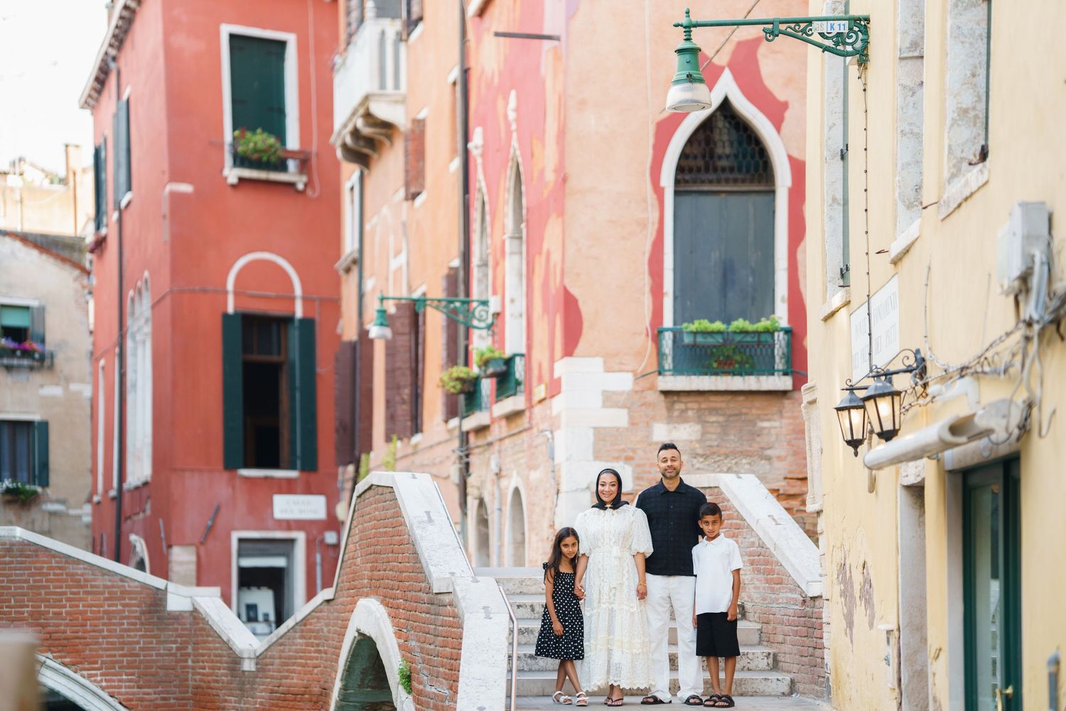 Family of four posing on a bridge in Venice, Italy, surrounded by colorful buildings and a canal.