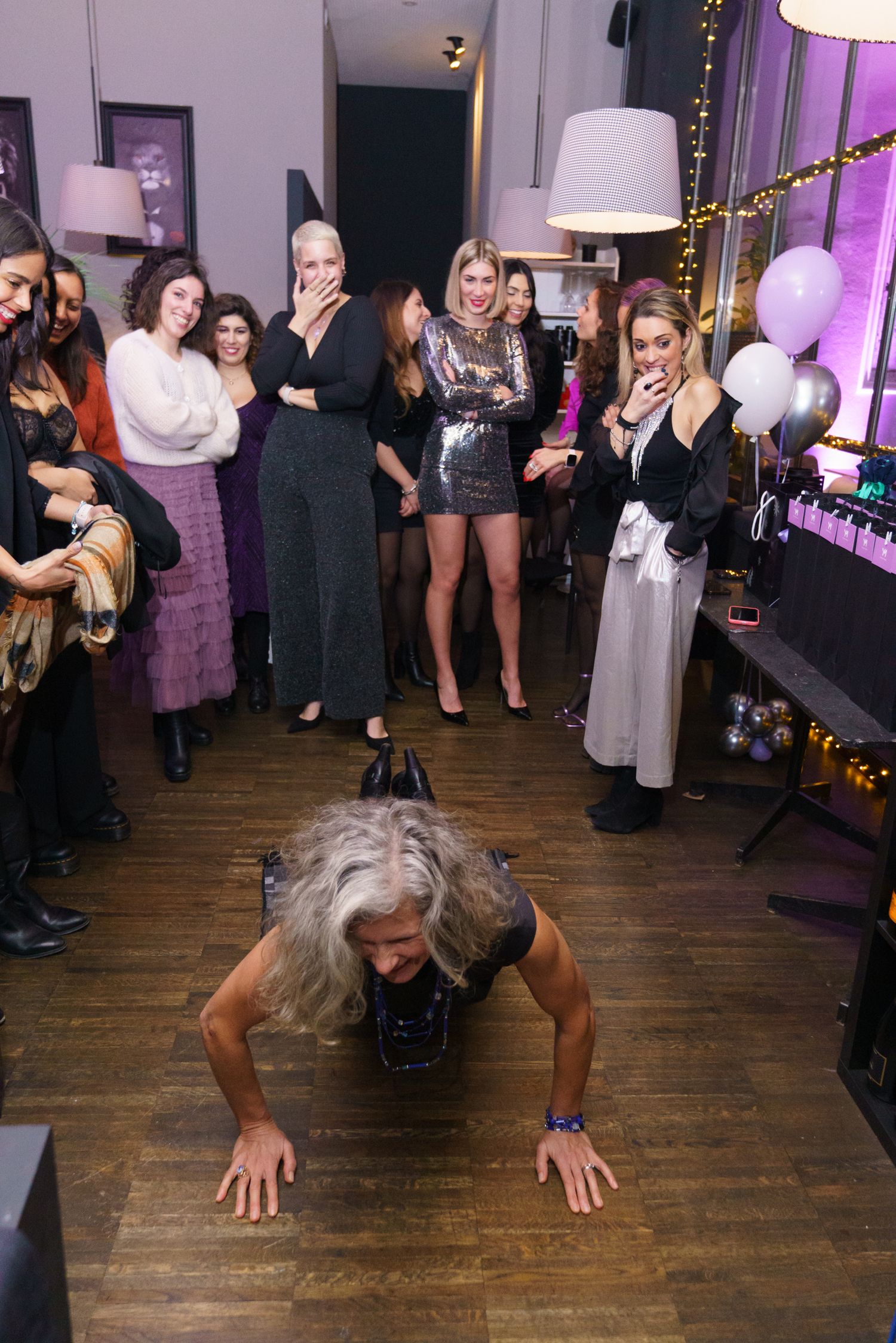 Woman doing push-ups at a party while guests laugh and watch in a decorated indoor venue.