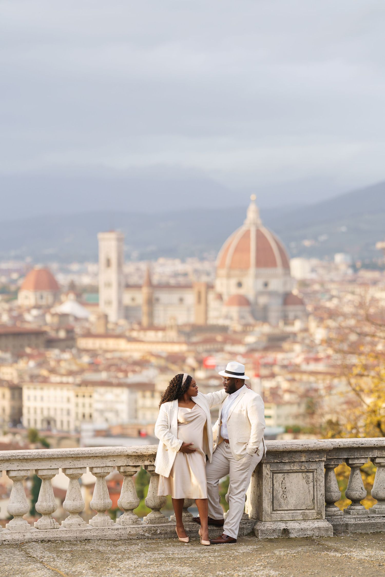 A couple in elegant white attire stands on a terrace overlooking the stunning Florence skyline with the iconic Duomo cathedral.