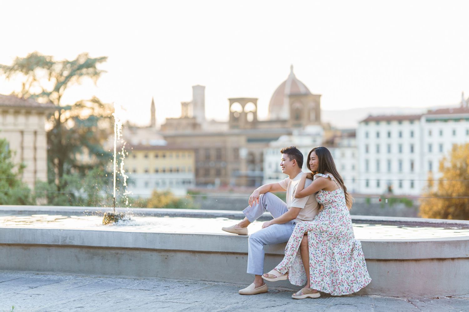 Couple sitting together by a fountain with Florence cityscape and cathedral dome in the golden hour background.