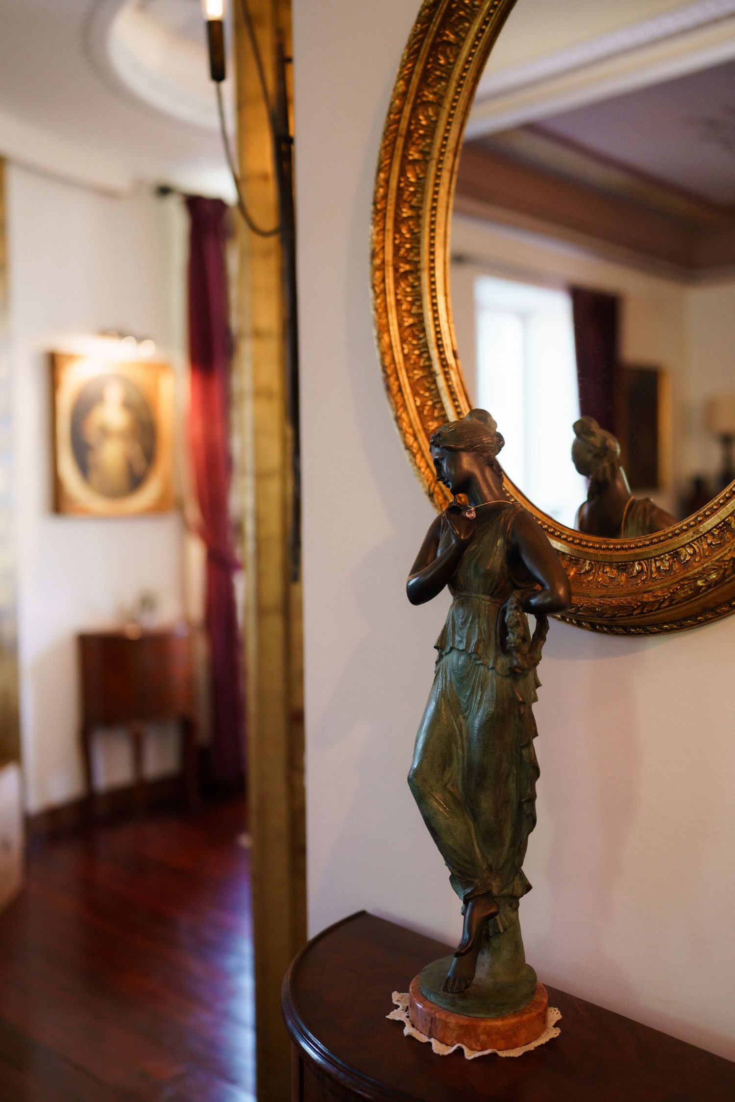 Antique bronze female figurine beside ornate gold circular mirror in elegant vintage interior room.