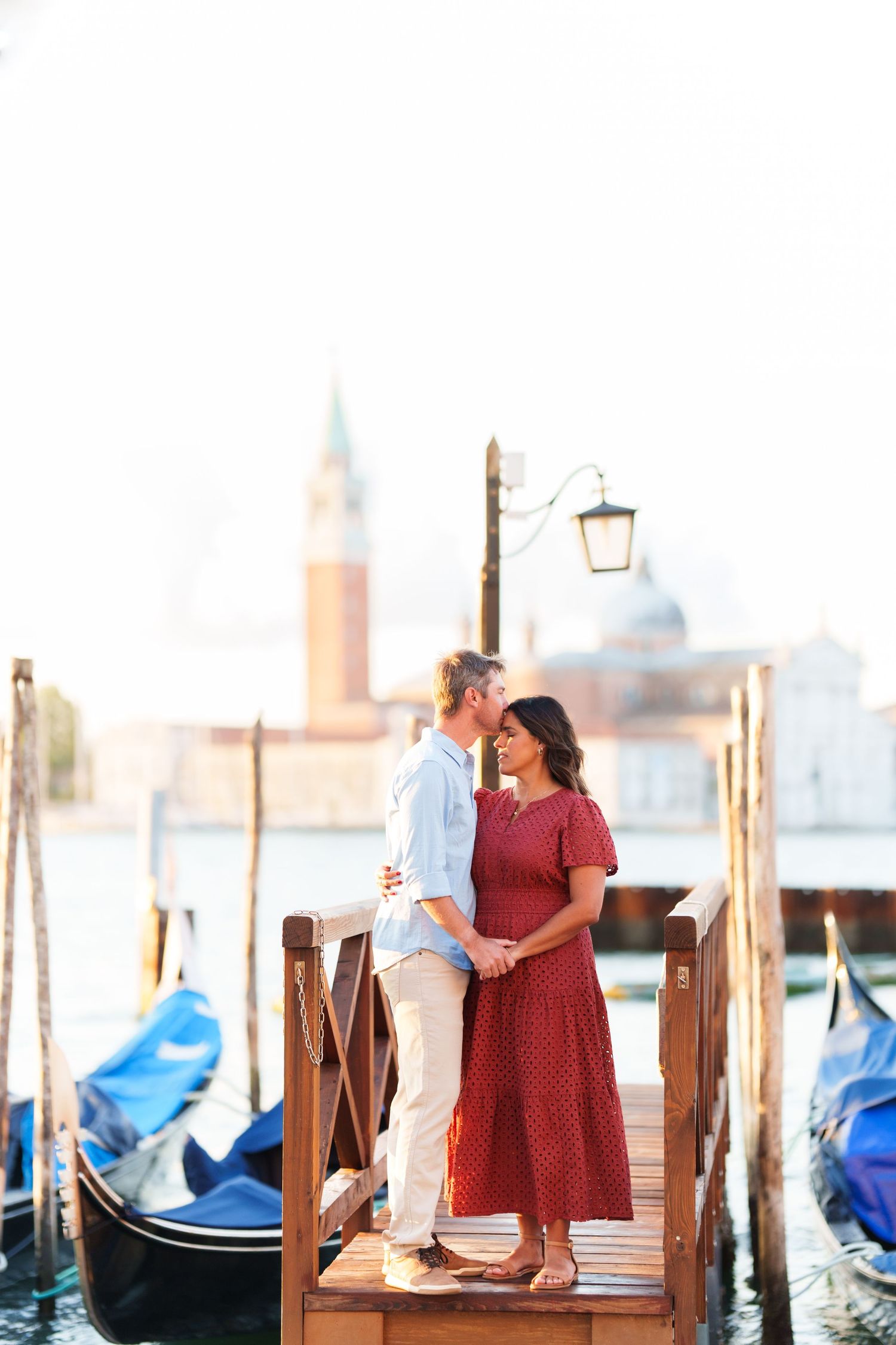 Romantic couple kissing on a Venice gondola dock with San Giorgio Maggiore church in the background.
