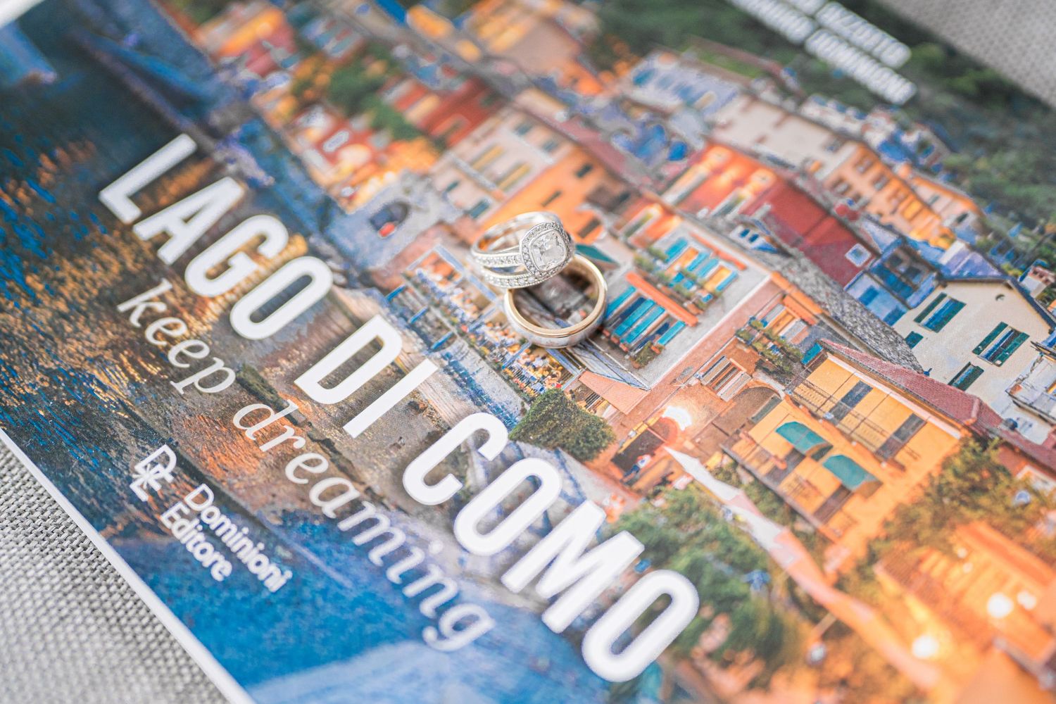 A Lago di Como travel book with a diamond ring resting on its colorful cover featuring Italian lakeside architecture.