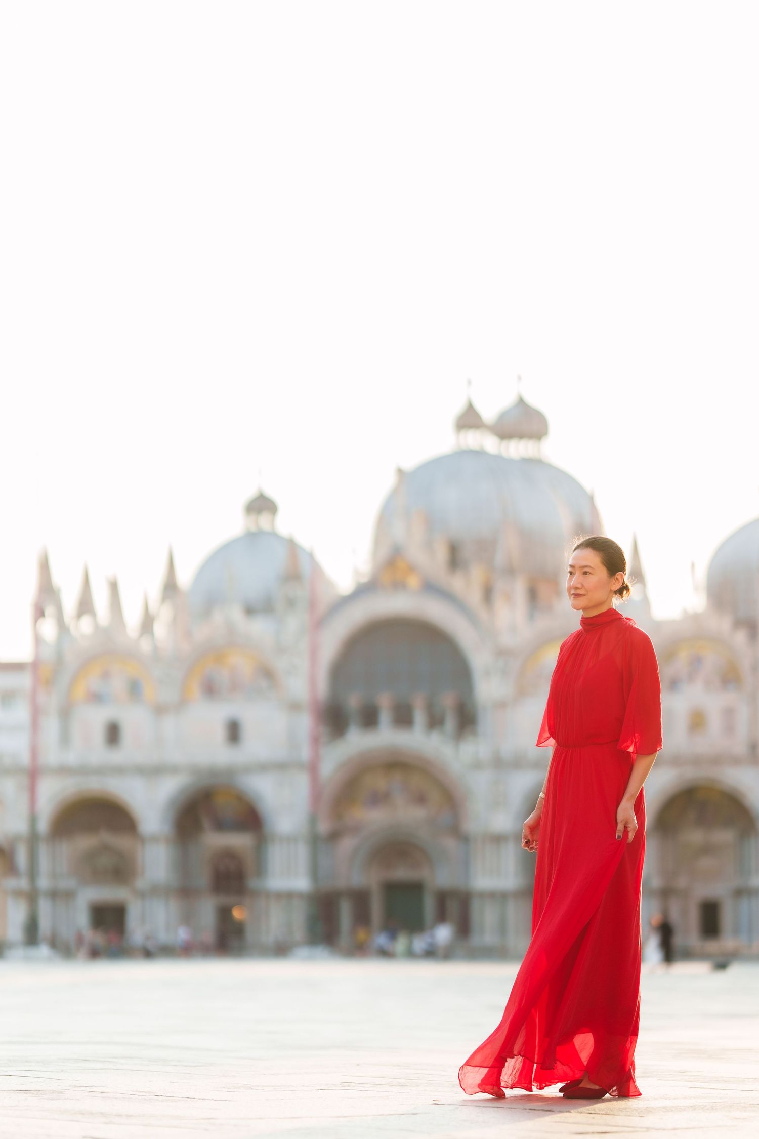 Woman in red gown poses in St. Mark's Square, Venice, with the iconic Basilica di San Marco in the background.