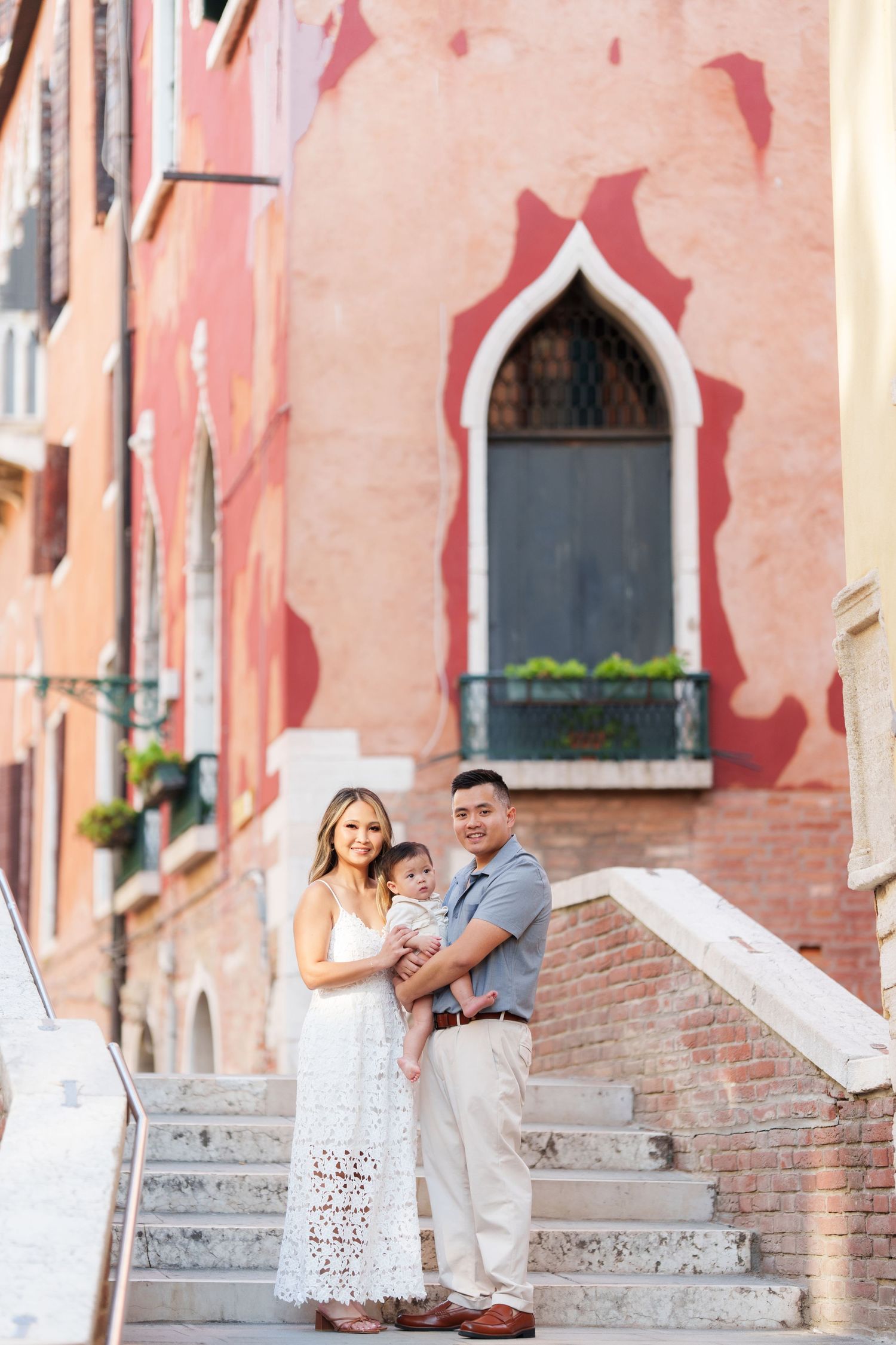Family posing on marble steps in Venice, Italy, with colorful historic buildings in the background.