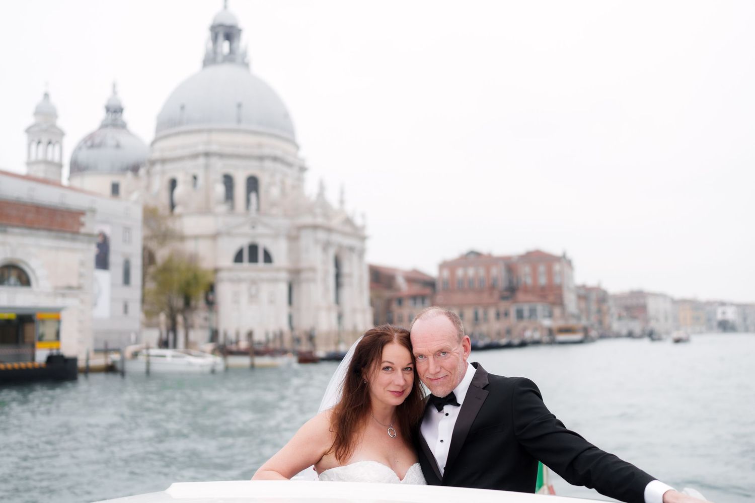 A romantic couple poses along Venice's Grand Canal with the Santa Maria della Salute church in the background.