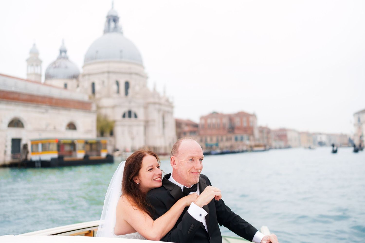 A couple shares a romantic moment in a gondola along the Venice canals with historic architecture in the background.