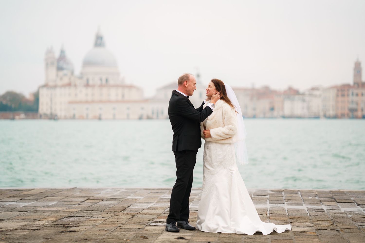 Romantic wedding couple shares tender moments along Venice's waterfront with San Giorgio Maggiore church in background.