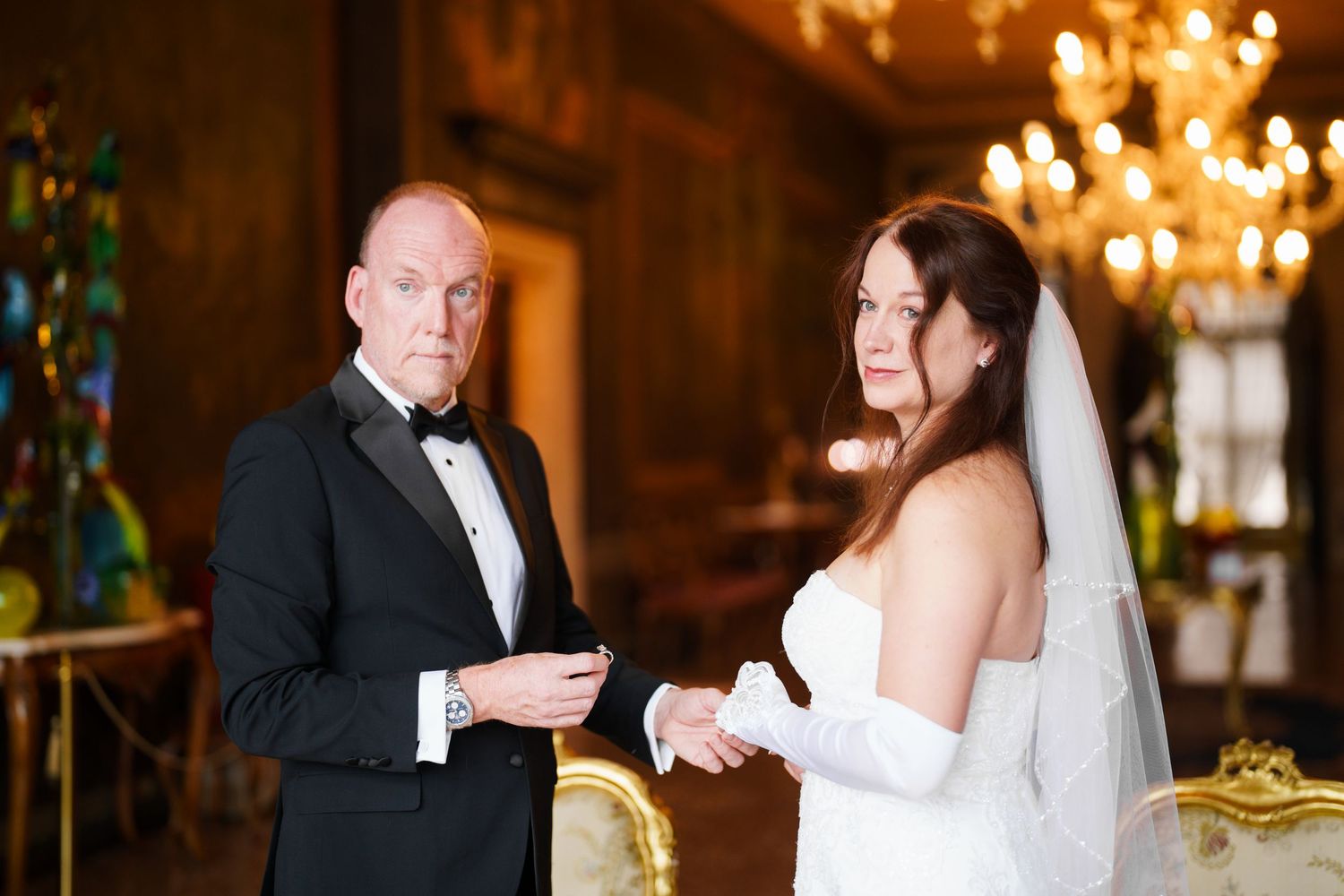 A couple shares an intimate moment during their wedding reception in an elegant ballroom with chandeliers.