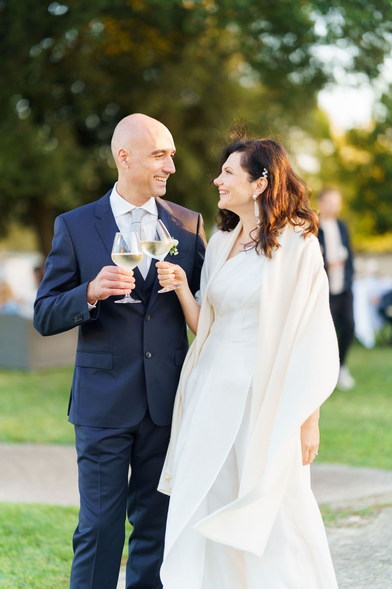 A couple toasts with wine glasses during their wedding celebration in a scenic outdoor setting.