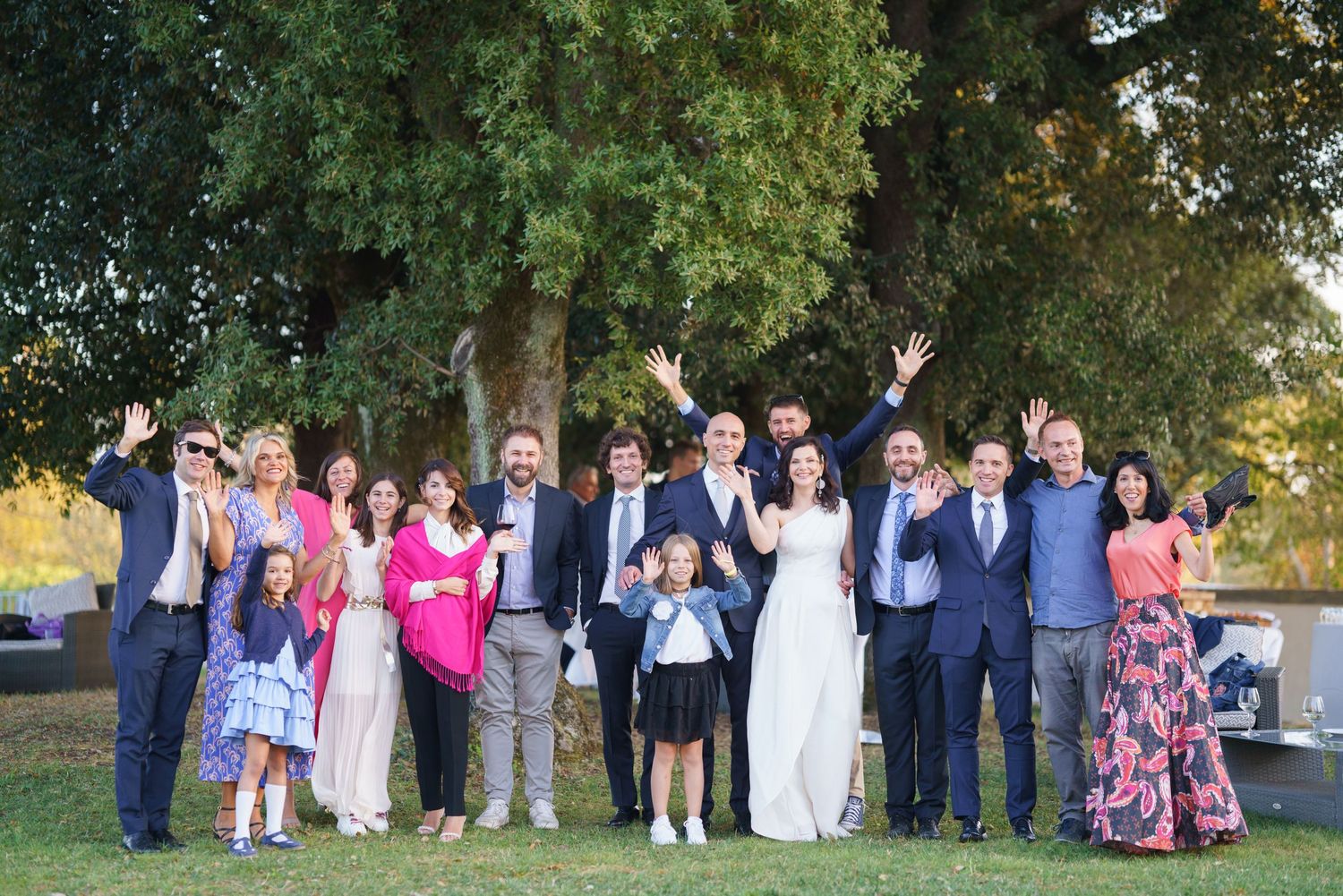 Wedding group portrait taken outdoors with trees and natural lighting.