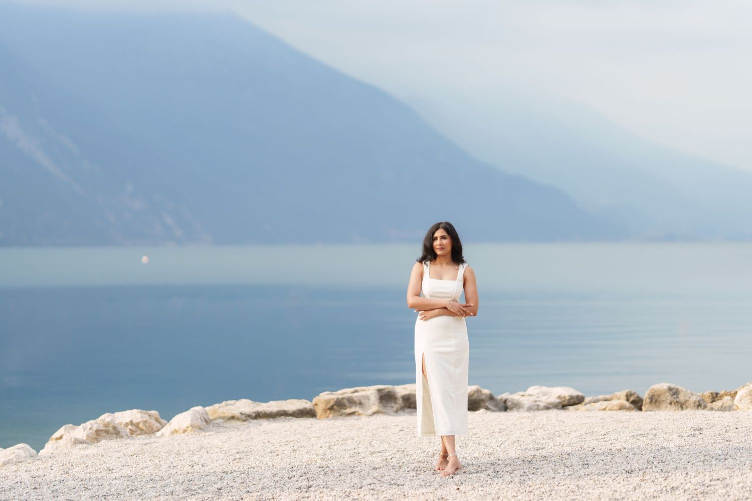 A panoramic view of a tranquil lake surrounded by misty mountains with white rocky shores in the foreground.